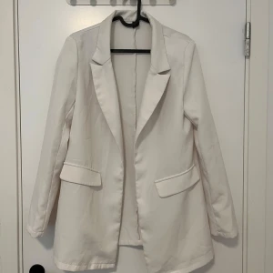 Vit kavaj med klassisk krage - Stilren vit kavaj med klassisk krage och två fickor framtill. Långärmad modell med rak passform och snygga detaljer vid fickorna. Perfekt för en clean och fräsch look.