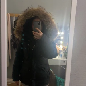 Svart jacka från Hollies -  svart jacka från Hollies med stor luva i storlek 32. Jackans dragkedja har gått av lite men går använda utan problem, den har många fickor och går att dra åt i midjan för bättre passform