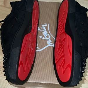 Christian Louboutin svarta sneakers(prisförslag)  - Svarta sneakers från Christian Louboutin i mocka med ikoniska röda sulor och svarta nitar på tån. Skorna har snörning och en platt sula. Perfekta för dig som vill sticka ut med en edgy och lyxig stil.