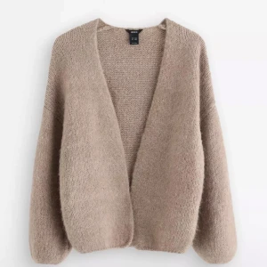 Beige stickad kofta från Lindex - Mysig beige stickad kofta från Lindex i oversized modell. Koftan har djup v-ringning, lång ärm och är tillverkad i ett fluffigt, mjukt material som passar perfekt för kyliga dagar. Enkel och stilren design som är lätt att matcha.