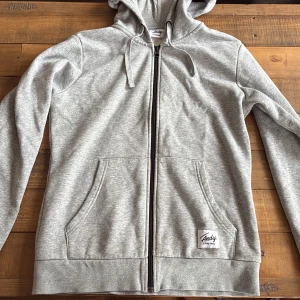 Grå hoodie från Andy by Frank Dandy - Snygg grå hoodie med dragkedja från Andy by Frank Dandy. Tröjan har huva med snörning, två stora fickor fram och ribbade muddar. Perfekt för chill dagar eller när du vill ha något bekvämt och stilrent.