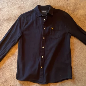 Mörkblå skjorta från Lyle & Scott - Snygg mörkblå skjorta. Skjortan är långärmad och tillverkad i 100% bomull. Lite tjockare material så funkar som en overshirt också. Nypris runt 500-700kr