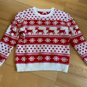 Jultröja med renar från dressforfun - Riktigt söt jultröja från dressforfun i rött och vitt med stickat mönster av renar, hjärtan och snöflingor. Tröjan är långärmad och har ribbade muddar vid hals, ärmslut och nederkant. Perfekt för att maxa julkänslan!