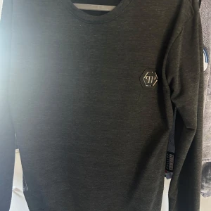 Svart långärmad tröja Philipp Plein - Svart långärmad tröja från Philipp Plein med rund halsringning och diskret logomärke på bröstet. Tröjan har en stilren look och är perfekt för dig som gillar minimalistisk design. Materialet känns mjukt och bekvämt mot huden. Väldigt lite använd