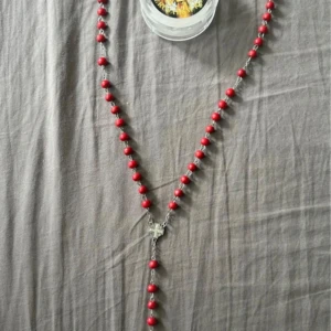 Rosenkrans halsband Jerusalem röd - Rosenkrans halsband med röda pärlor och detaljer i silverfärgad metall. Korset har en Jesusfigur och en medaljong med texten 'Jerusalem'. Tillverkad, Inköpt och helgad i Jerusalem. Kommer i en ask med St.Maria och helige familjen bild och bön . Perfekt för dig som vill ha något unikt, meningsfullt och heligt .