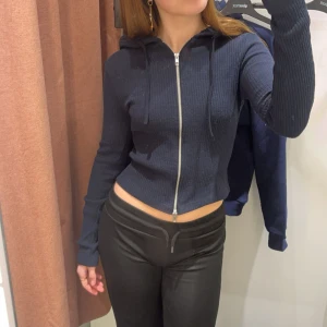 Mörkblå croppad hoodie med dragkedja - Säljer en mörkblå croppad hoodie med dragkedja framtill och huva. Tröjan är ribbad och är från ginatricot.