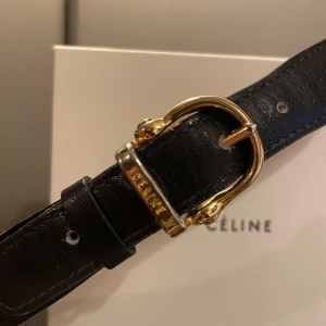 Celine bälte  - Äkta Celine bälte. Design: Celine Färg: Marinblå m guldspänne Storlek: 75cm exkl knäppe Skick: finns skavmärken på bältet, se bilderna. Helhetsintrycket är väldigt fint, stelt i formen. Köp på Tradera kvitto därifrån.  75 cm, yttersta hål 73 cm 