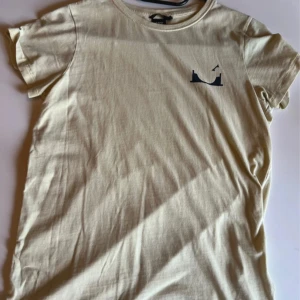 Gul t-shirt från Lager157 med tryck - Beige t-shirt från 157 med coolt svart tryck framtill och stort grafiskt tryck på ryggen med texten 'spinning around all the time'. Klassisk rund hals och korta ärmar. Skön och mjuk i bomull, perfekt för en avslappnad stil.