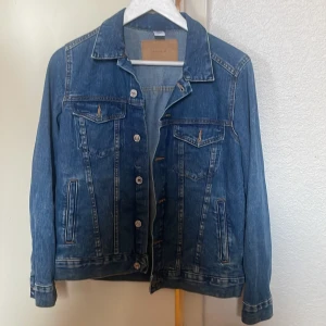 Blå jeansjacka från Studio - Klassisk blå jeansjacka från Studio med silverfärgade knappar, två bröstfickor med lock och två sidofickor. Jackan har en rak passform och krage, perfekt för att lyfta vilken outfit som helst.