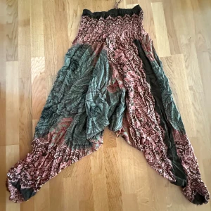 Blommiga vida harembyxor med bred resår i midjan och  snörning - Säljer ett par superbekväma harembyxor med blommigt mönster i grönt och rosa. Byxorna har bred resår i midjan och vid benslut samt snörning upptill. Luftigt material, perfekt för varma dagar, yoga eller chill hemma. Unik boho-vibe och loose fit.