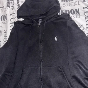 Svarta mjukisbyxor från Polo Ralph Lauren - Äkta Ralph Lauren tracksuit. Svart zip tröja & mjukisbyxor från Polo Ralph Lauren med klassisk vit logga broderad på benet. Byxorna har snörning i midjan och är tillverkade i mjukt bomullsmaterial. Perfekta för en chill och avslappnad stil.