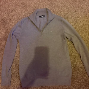 Grå half zip tröja från J.Lindeberg - Snygg grå stickad tröja från J.Lindeberg med halv dragkedja. Tröjan har diskret broderad logga på bröstet och ribbade muddar vid ärmslut och nederkant. När jag köpte den så var den i storlek M men sen råkade jag tvätta den för varmt så det blev storlek S istället. Därför är priset så pass lågt. Ny pris 1500kr mitt pris 369kr