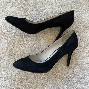 Svarta mockapumps från Pier One 40 - Klassiska svarta pumps från Pier One i mocka med spetsig tå och hög klack. Snygg och tidlös modell som passar till många olika looks. Insidan är ljus och mjuk för extra komfort. Perfekta för dig som gillar stilrena och eleganta skor.