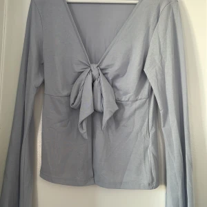 Ljusblå  långärmad topp med knyt Gina Tricot - Supersnygg ljusblå  långärmad topp från Gina Tricot med djup v-ringning och knyt framtill. Toppen är i mjuk bomullsmix och har en clean, enkel look som passar perfekt till jeans eller kjol. Snygg croppad passform och stilren design.