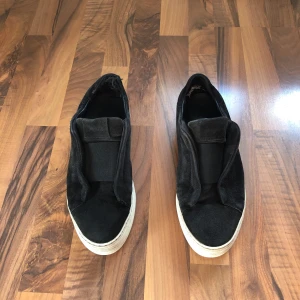 Svarta Axel Arigato skor - Svarta slip-on sneakers från Axel Arigato i mocka med vit platt sula. 