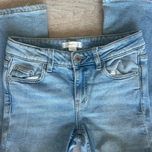 Bootcut jeans barn i ljusblå denim Gina Tricot! - Bootcut jeans från Gina Tricot i ljusblå tvättad denim. Klassisk femficksmodell med normal midja och utsvängda ben. Jeansen har bälteshällor, knapp och dragkedja framtill. Perfekta för en avslappnad och trendig look.