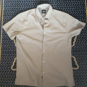  Kortärmad skjorta - Snabb leverans! 🚚 Dm för fler bilder! Aldrig använd, ny utan tag! Snygg beige skjorta från R&B i regular fit med korta ärmar och klassisk krage. Skjortan har knäppning framtill med vita knappar och är tillverkad i ett mjukt bomullstyg. Perfekt för en clean och stilren look.