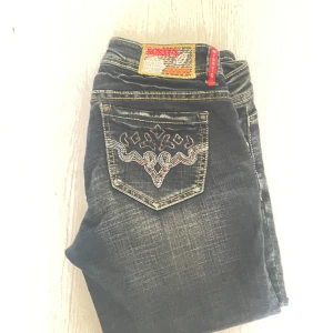 Missy’s croppade jeans med broderi - Mörkblå croppade jeans från Missy’s med snygga slitningar och broderade detaljer på fickorna. Jeansen har dekorativa knappar vid benslut och kontrastsömmar som ger en cool look. Perfekta för dig som gillar unika detaljer och streetstyle.