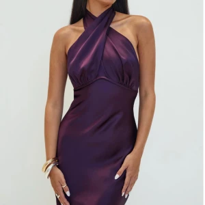 Lång lila satinklänning med öppen rygg - Säljer en elegant långklänning i glansigt lila satin med halterneck och snygg omlott-detalj framtill. Klänningen har öppen rygg med knytband och figurnära passform som ger en lyxig känsla. Köpt från princesspolly och i perfect skick!