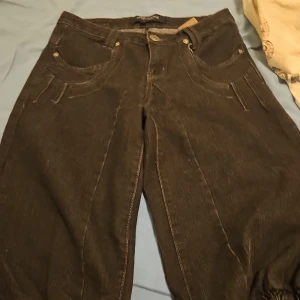 Bruna jeansbyxor från Marc Lauge - Snygga bruna jeansbyxor från Marc Lauge med klassisk femficksdesign och coola sömdetaljer. Byxorna har raka ben och kontrastsömmar som ger en schysst look. Perfekta för dig som gillar en stilren men ändå unik vibe.