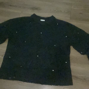 Svart stickad polotröja med paljetter - Mysig svart stickad polotröja med glittriga paljettdetaljer över hela tröjan. Perfekt för dig som vill ha en enkel men ändå festlig look. Tröjan har lång ärm och hög krage som ger en cool vibe.