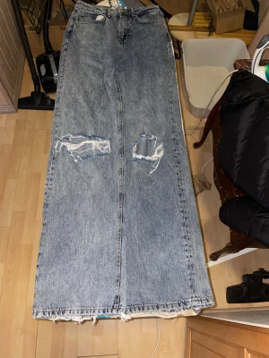 Jeans från NA-KD, storlek 34 - Säljer ett par  jeans från NA-KD i klassisk blå denim. Byxorna har slitna detaljer och hål på framsidan,har fickor både fram och bak. Perfekt för dig som gilla en avslappnad stil.