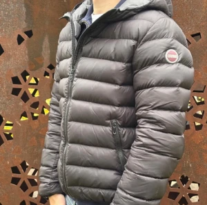 Svart dunjacka från Colmar med huva - Säljer en svart dunjacka från Colmar med huva och dragkedja framtill. Jackan har en quiltad design, två sidofickor med dragkedja och en rund Colmar-logga på ärmen. Perfekt för kyliga dagar och riktigt snygg passform.