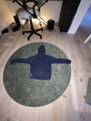 Marinblå hoodie från Polo Ralph Lauren - Säljer en marinblå hoodie från Polo Ralph Lauren i storlek M(10-12). Tröjan har dragkedja framtill, huva och det klassiska röda Polo-logot broderat på bröstet. Tillverkad i mjuk bomull, perfekt för chill dagar eller när du vill ha en clean och enkel look. An