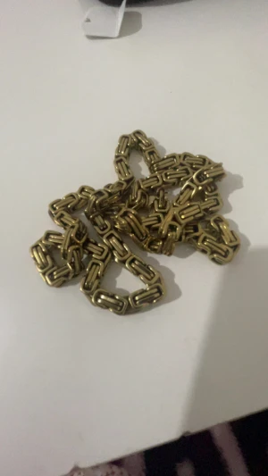 Tung guldfärgad kedja i metall - Säljer en chunky guldfärgad kedja i metall med rektangulära länkar och karbinlås. Kedjan har en cool, robust design som sticker ut och passar perfekt för dig som gillar statement-accessoarer.