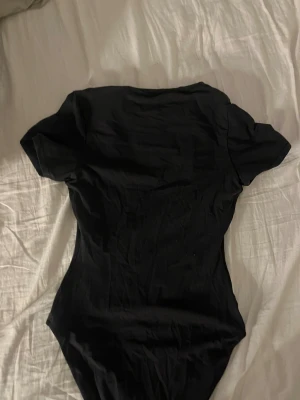 mörkgrå kortärmad body - En enkel mörkgrå body med korta ärmar och figurnära passform. Perfekt att styla med jeans eller kjol för en clean look. Tunt och mjukt material som känns skönt mot huden. från skims och i bra skick därav pris 