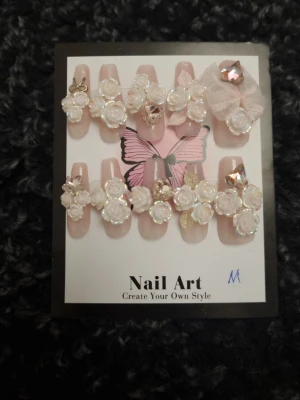 Lyxiga  press-on naglar med rosor Strl M - Mediumlånga press-on naglar i ljusrosa med 3D vita rosor, rosetter och strass,                   Mått( båda vänster och höger är samma )  Tumme =    1,7 cm bredd längd    3 cm Pekfinger =   1,5 cm bredd längd 2.7 cm Långfinger = 1,5 cm bredd längd 2.7 cm Ringfinger = 1,5 cm bredd längd 2.7 cm Lillfinger =   1, 3 cm bredd  längd 2.6  cm      OBS! Storleken är baserad på manuell mätning och kan variera med 1-2 cm