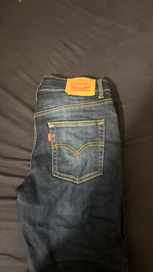 Levi's 512 Slim Taper jeans mörkblå - Mörkblå Levi's 512 Slim Taper jeans med klassiska gula sömmar och femficksdesign. Jeansen har en smal passform med avsmalnande ben och är tillverkade i slitstarkt denim. Perfekta för dig som gillar en modern och clean look. 