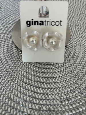 Pärlörhängen i blomform Gina Tricot - Säljer ett par snygga örhängen från Gina Tricot med pärla i mitten och blomformad design. Färgen är vit med skimrande yta, och materialet är plast med pärlimitation. Perfekt för dig som vill ha en söt och trendig detalj till din look.