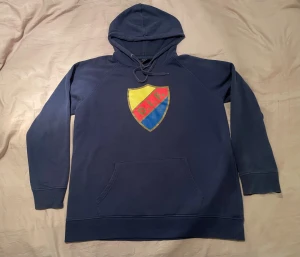 DIF Hoodie storlek Large (L) - Mörkblå hoodie i Storlek L med Djurgårdens IF logotyp tryckt på bröstet. Den har en ficka på magen och muddar i ärmslut och nederkant. Inte i nyskick.   Säljer denna billigare än vanligt då den är välanvänd och tvättad många gånger, men trots det relativt välbevarad. Speciellt DIF-loggan är välbevarad, vilket ger hopp att den håller många år till om man är noggrann med hur man tvättar den. Finns lite noppor på sina ställen om man tittar noga, men inget som stör. Kolla noga på bilder innan köp. 