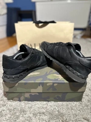 Valentino Rockrunner svarta sneakers - Svarta Valentino Rockrunner sneakers med coola nitar på sulan. Skorna har en mix av skinn och mocka, samt snörning framtill. Snygg och stilren design som ger en edgy vibe. Perfekt för dig som gillar exklusiva märken och streetstyle. Strl 45. Box medföljer ej men kan förhandlas