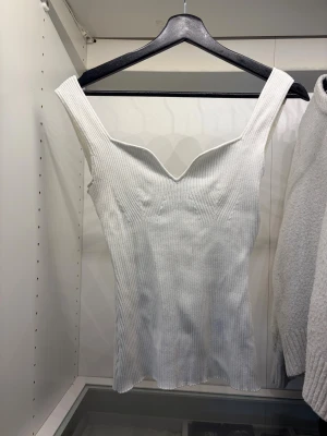 Vit ribbad linnetopp med v-ringning - Säljer en vit ribbad linnetopp med breda axelband och snygg v-ringad hals. Toppen är figurnära och har en stilren, modern look som är enkel att matcha. Färgen är vit/cremevit.
