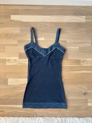 Mörkblå linnetopp med spets från Abercrombie - Supersnygg mörkblå linnetopp från Abercrombie & Fitch i ribbad bomull. Toppen har tunna axelband och v-ringad spetskant både upptill och nedtill. Liten broderad logga vid nederkanten. Perfekt för dig som gillar stilrena detaljer och mjuka material.