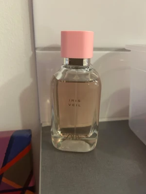 ZARA Iris Veil parfym - Modern parfym från ZARA med stilren design och rosa tonad vätska. Perfekt för dig som vill ha en trendig accessoar på hyllan. Namnet 'Iris Veil' syns tydligt på flaskan.