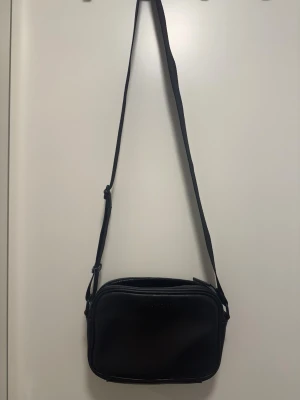 Svart axelväska från Valentino - Snygg svart axelväska från Valentino med stilren, rektangulär form och justerbar rem. Väskan är tillverkad i skinn och har diskret logga på framsidan samt flera fack med dragkedja inuti. Perfekt för dig som gillar minimalistisk design och vill ha plats för det viktigaste. Kom med prisförslag, priset är inte fast 