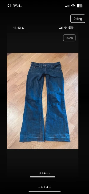 Blå lågmidjade bootcut jeans med broderad ficka - Snygga mörkblå lågmidjade jeans med bootcut passform och coola broderade detaljer på bakfickan. Jeansen har klassisk femficksdesign, kontrastsömmar och knappar i olika färger. Materialet är jeans och de har en unik patch på ena bakfickan.