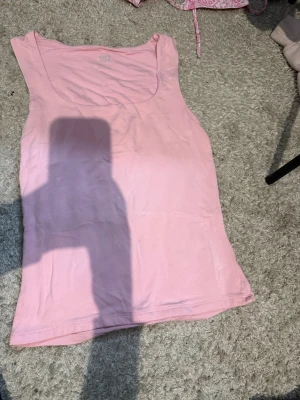 Ljusrosa linne från 157 - Säljer ett ljusrosa linne från 157 med klassisk rund halsringning. Toppen är ärmlös och gjord i mjuk bomull, perfekt för varma dagar eller som lager under andra plagg. Enkel och stilren design som funkar till många olika looks.