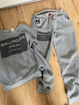 Grå mjukisbyxor Ballinciaga Harlem - Snygga grå mjukisbyxor från Ballinciaga Harlem med tryck på benet och rosa snörning i midjan. Sköna och avslappnade med elastisk midja och muddar vid benslut. Perfekta för chill eller häng med kompisar.