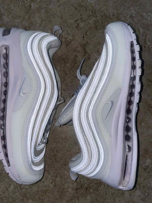 Nike Air Max 97 Triple White sneakers - Nike Air Max 97 Triple White sneakers i storlek 44. Snyggt vågigt mönster med reflekterande detaljer, vit ovandel i mesh och syntet, samt den ikoniska Air Max-sulan. Perfekta för dig som gillar stilrena och sportiga sneakers med maxad komfort.