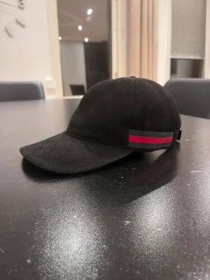 SÄLJER EN GUCCI CAP  - Hej. Jag säljer en gg canvas cap från Gucci den är äkta och säljer den på ground av att behöver pengar Säljer en svart keps från Gucci med klassiskt GG-monogram över hela kepsen. Sidan har den ikoniska gröna och röda randen. Justerbar rem baktill i skinn. Snygg och stilren accessoar för dig som gillar lyxiga detaljer.