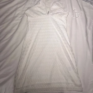 Vit miniklänning från Hm - Supersöt vit kort klänning från H&M Divided med halterneck och v-ringning. Klänningen har ett vackert spetsmönster över hela och är fodrad. Perfekt som strand klänning, den är lite syd vid brösten🩷