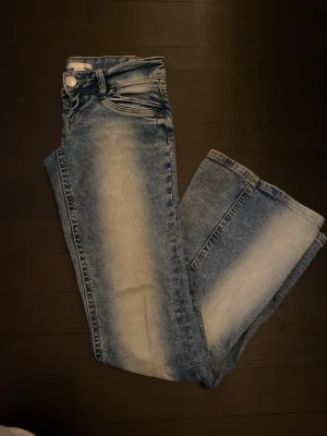 Blå jeans med blekta detaljer - Säljer ett par blå jeans med coola blekta partier längs benen. Klassisk femficksmodell med knapp och dragkedja framtill. Jeansen har en rak passform och är tillverkade i jeansmaterial. Perfekt för dig som gillar en avslappnad och trendig look.