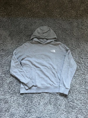 Grå hoodie från The North Face XL - Säljer en stilren grå hoodie från The North Face i storlek XL för tonåringar. Tröjan har huva, ribbade muddar och en klassisk magficka. Materialet är mjuk bomull och polyester, perfekt för chill dagar. Diskret logga på bröstet för en clean look.