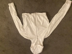 Vit hoodie med dragkedja från H&M - Vit hoodie från H&M i storlek 170. Tröjan har hel dragkedja framtill, två fickor och en huva. Tillverkad i mjuk bomullsmix med ribbade muddar vid ärmslut och nederkant. Perfekt för chill dagar och enkel att matcha med jeans eller joggers.