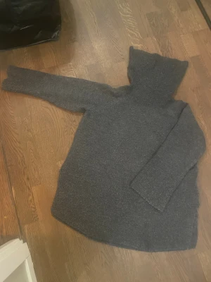 Mörkgrå stickad polotröja oversize - Mysig mörkgrå stickad polotröja med hög krage och långärmad design. Tröjan har en loose passform och är perfekt för kyliga dagar. Materialet är grovstickat och känns riktigt skönt mot huden. Enkel och stilren look som funkar till jeans eller mjukis.