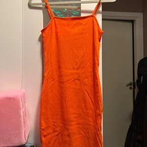 Orange ribbad klänning med smala axelband - Snygg orange klänning med smala axelband och ribbad struktur. Modellen är kroppsnära och har en rak, enkel design som ger en cool och trendig vibe. 